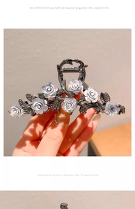Close-up of a dark metal hair claw clip with white roses and diamond embellishments
