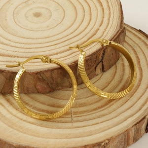 Golden titanium steel hoop earrings with Greek key pattern on a wooden background