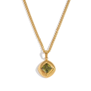 Close-up of gold chain necklace with textured rhombus pendant and green square gemstone