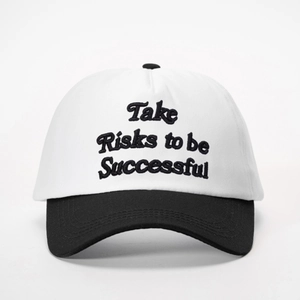 Detail shot of Take Risks to be Successful embroidery on white and black baseball cap