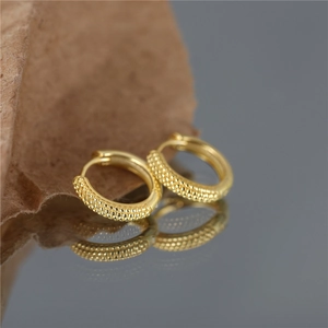 Macro shot of gold-plated S925 silver hoop earrings with embossed dot texture on a mirror