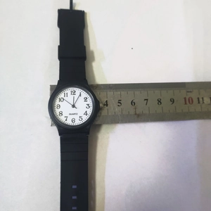 Detail view of the 3.3cm diameter black quartz watch dial measured with a metal ruler