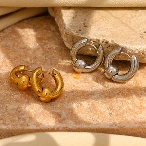 Detail of beaded huggie hoop earrings in gold and silver finish on textured stone surface