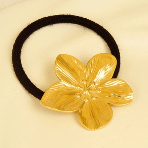 Detail of a golden metal flower on a black elastic hair tie with textured petals