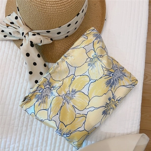 Detailed close-up of a floral jacquard makeup bag with a summer straw hat on a quilted bed