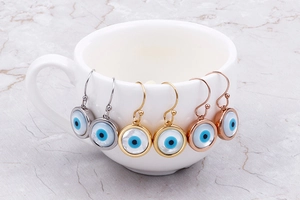 Three pairs of evil eye drop earrings in silver, gold, and rose gold plating on a cup