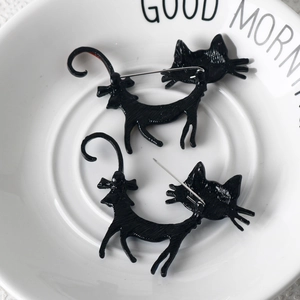 Close-up of two black enamel cat brooches on a white plate with fine metal textures