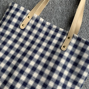 Detailaufnahme der blau-weiß karierten Canvas-Tasche mit Ledergriff und Nieten