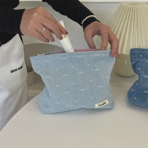 Close-up of denim cosmetic bag with bow patterns showing pink lining and zipper closure