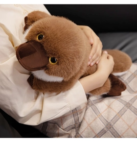 Close-up of a soft brown plush platypus toy being held by a model in a warm setting