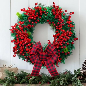 Christmas wreath with green pine needles, red berries and a plaid bow on white wood