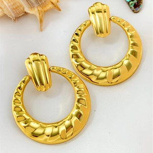 Retro golden geometric hoop earrings with textured ripple finish on white fabric