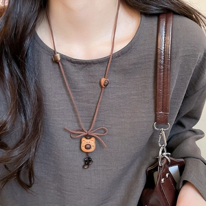 Close-up of wooden bead bear pendant necklace on leather cord over grey fabric
