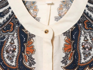 Detail eines Stehkragens mit Paisley-Muster und goldenem Knopf am Damenkleid