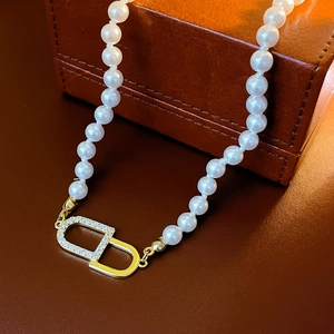 Gros plan d'un collier de perles avec pendentif logo CD doré et zircons brillants