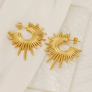 Golden sunburst C-shaped stud earrings with radiant metal spikes on white marble