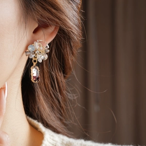 Detail view of flower-shaped earrings with crystal petals and purple gemstone drop