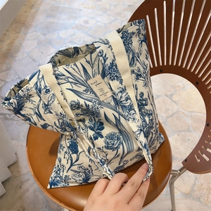 Close-up of cream canvas tote bag featuring blue vintage plant prints on a leather chair