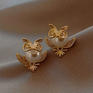 Macro shot of owl stud earrings with white faux pearls and shimmering gold plating