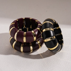 Detail of burgundy and black acrylic bracelets with gold metal separators on white background