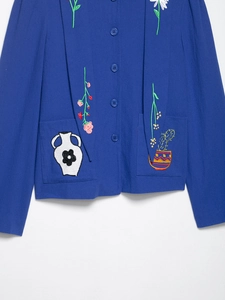 Detail of blue textured shirt featuring floral embroidery and patch pockets