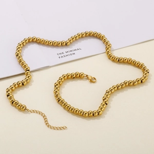 Détail d'un collier à billes en acier doré avec fermoir mousqueton sur un livre épuré