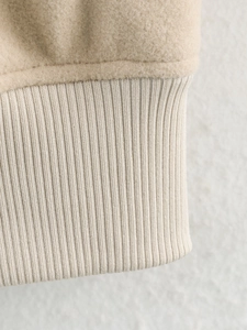 Detailed close-up of beige fleece fabric and ribbed knit cuff on casual winter jacket