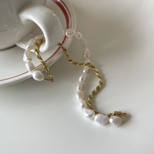 Detailed shot of baroque pearl and golden twisted chain draped on a ceramic coffee cup