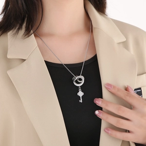 Close-up of a silver key pendant necklace with crystal encrusted double rings on a model
