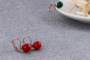 Détail de boucles d'oreilles dormeuses or rose avec perles rouge et vert poli