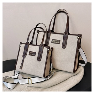 Detail view of contrast canvas tote bags with brown leather trim and striped shoulder strap