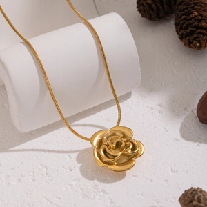 Macro shot of an elegant golden rose pendant with a snake chain on a white textured base