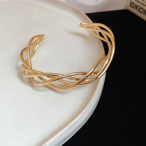 Macro detail of gold twisted multi-strand metal cuff bracelet on ceramic plate