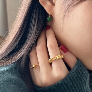 Close-up of a model wearing a gold twisted ring and beaded earrings with a green knit top