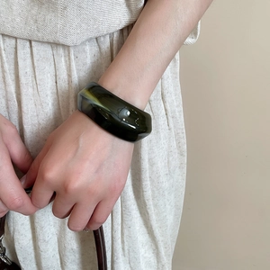 Close-up of wide acrylic marble bangle with dark green and yellow patterns on wrist