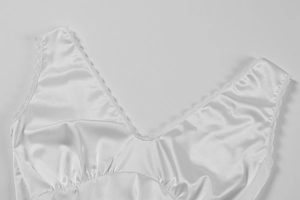 Detail of V-neck white satin dress with delicate lace trim and pleated bust texture