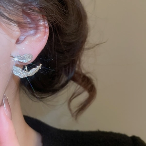Macro view of silver feather earrings with pavé zircons worn on model's ear
