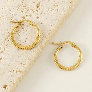 Golden titanium steel hoop earrings with vertical texture on natural travertine stone