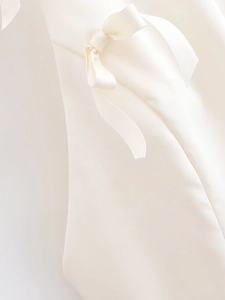 Detail of a white woven fabric top featuring a delicate handmade bow tie decoration
