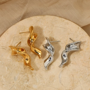 Polished gold and silver twisted geometric earrings on a marble display tray