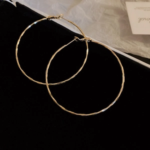 Detailed view of large gold hoop earrings with hammered metal texture on black velvet