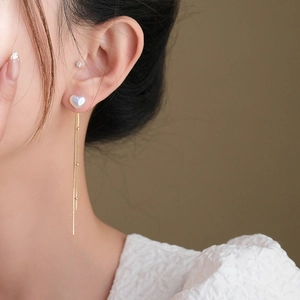 Elegant pearl heart dangle earrings with long gold tassels on a model's ear