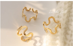 Three gold U-shaped wavy open rings in polished titanium steel on a white surface