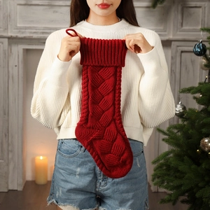 Red knitted Christmas stocking with classic cable pattern held in festive home setting