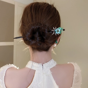 Detail of vintage flower hair pin with green jade-like petals and pearl tassels on a bun