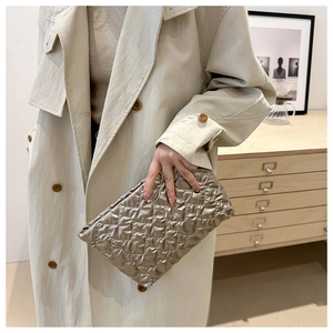Champagne gold quilted clutch bag with metallic texture held by a model in a beige coat