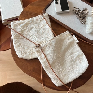 Close-up of beige linen crossbody bags with leaf embroidery and leather strap detail