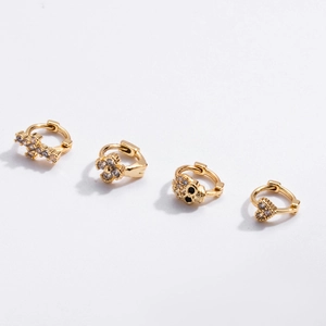 Gold huggie earrings set with zircon cross, clover, skull, and heart charms on white background