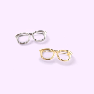 Creative eyeglasses-shaped metal brooches in gold and silver colors on purple background