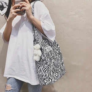 Detail of zebra pattern canvas tote bag with a plush bear charm worn by a model